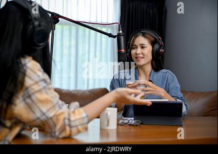 Schöne junge asiatische weibliche Podcast Radio-Host genießt interviewen ihren besonderen Gast in ihrem Heimstudio. Zwei Podcasters in Kopfhörern lachen, Talki Stockfoto