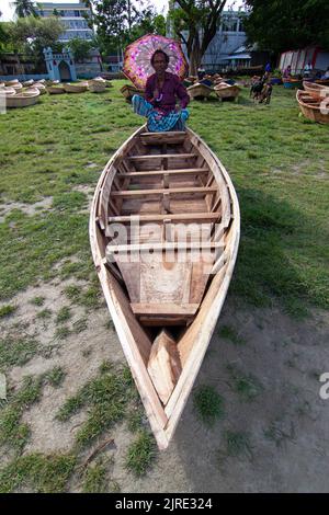 Manikganj, Dhaka, Bangladesch. 24. August 2022. Ein Verkäufer sitzt mit einem Regenschirm über seinem Boot, um es auf Bangladeshs größtem Bootsmarkt in Manikgonj, Bangladesch, zu verkaufen. Wird von den Einheimischen während des Monsuns verwendet Wenn starke Niederschläge das Flussufer zum Platzen bringen, kostet jedes Schiff zwischen Â£30 und Â£80, abhängig von seiner Größe und der Qualität der verwendeten Materialien. Die Menschen strömten auf den Freiluftmarkt, um Boote zu kaufen, um sich auf die kommende Regenzeit vorzubereiten. Kredit: ZUMA Press, Inc./Alamy Live Nachrichten Stockfoto