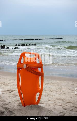 Ein orangefarbenes Rettungsboot steckte im Sand am Strand fest. Im Hintergrund ein Blick auf das Meer und die Wolken am Horizont Stockfoto