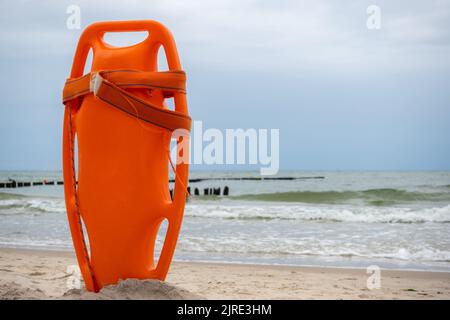 Ein orangefarbenes Rettungsboot steckte im Sand am Strand fest. Im Hintergrund ein Blick auf das Meer und die Wolken am Horizont Stockfoto