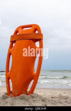 Ein orangefarbenes Rettungsboot steckte im Sand am Strand fest. Im Hintergrund ein Blick auf das Meer und die Wolken am Horizont Stockfoto