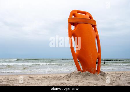 Ein orangefarbenes Rettungsboot steckte im Sand am Strand fest. Im Hintergrund ein Blick auf das Meer und die Wolken am Horizont Stockfoto