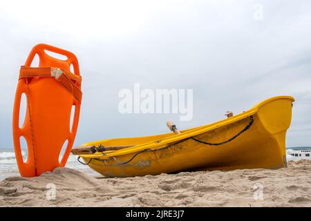 Ein orangefarbenes Rettungsboot steckte im Sand am Strand fest. Im Hintergrund ein Blick auf das Meer und die Wolken am Horizont Stockfoto