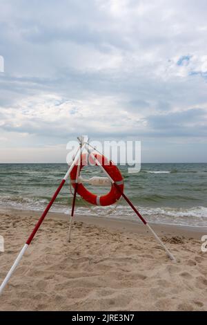 Ein orangefarbenes Rettungsboot und REACH-Extender stecken im Sand am Strand. Im Hintergrund ein Blick auf das Meer und die Wolken am Horizont Stockfoto