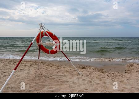 Ein orangefarbenes Rettungsboot und REACH-Extender stecken im Sand am Strand. Im Hintergrund ein Blick auf das Meer und die Wolken am Horizont Stockfoto