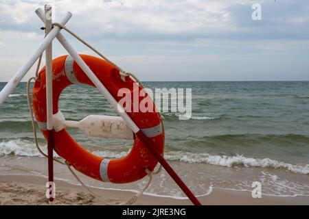 Ein orangefarbenes Rettungsboot und REACH-Extender stecken im Sand am Strand. Im Hintergrund ein Blick auf das Meer und die Wolken am Horizont Stockfoto