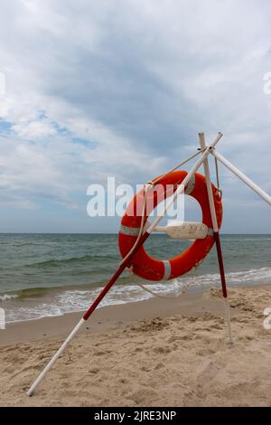 Ein orangefarbenes Rettungsboot und REACH-Extender stecken im Sand am Strand. Im Hintergrund ein Blick auf das Meer und die Wolken am Horizont Stockfoto