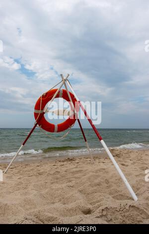 Ein orangefarbenes Rettungsboot und REACH-Extender stecken im Sand am Strand. Im Hintergrund ein Blick auf das Meer und die Wolken am Horizont Stockfoto