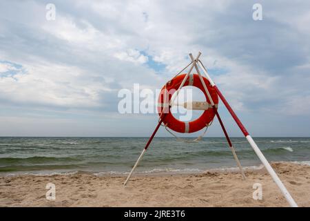 Ein orangefarbenes Rettungsboot und REACH-Extender stecken im Sand am Strand. Im Hintergrund ein Blick auf das Meer und die Wolken am Horizont Stockfoto