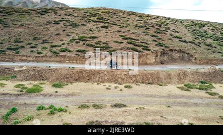 Mann auf einem Motorrad, der Spiti Valley auf der ländlichen Schotterstraße von Himachal Pradesh bereist Stockfoto