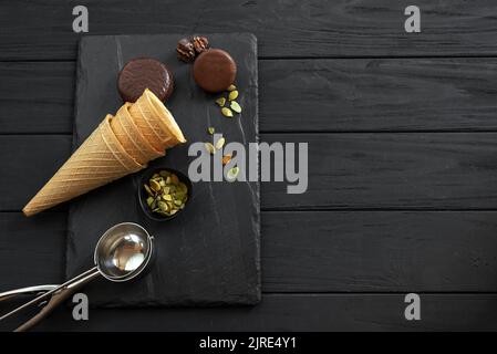 Zutaten für Cookies N' Cream Eis mit Schokolade und Keksen, Nüssen, Zuckerzapfen, Kübeln und einer Metalllöffel auf einem Schiefer, Draufsicht Stockfoto