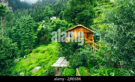 Männlicher Tourist auf dem Balkon des schönen hölzernen winzigen Baumhauses in den Bergen von Jibhi Indien an bewölktem Tag Stockfoto