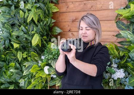 Fröhliche glückliche Frau, die im Freien in der Stadt mit der Kamera fotografiert. Schöne asiatische Frau Fotograf halten Fotokamera. Eine Journalistin sh Stockfoto
