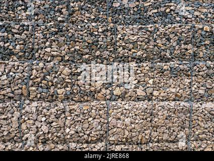 Gabion mit Haufen kleiner Steine in einem Gitter als Stadt- oder Gartendekoration, strukturierter Hintergrund Stockfoto