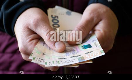 Weißer Mann zeigt ukrainische Griwna-Scheine in seiner Hand in Nahaufnahme Vorderansicht Stockfoto