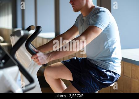 Nahaufnahme eines jungen Muskelmannes, der im Fitnessstudio an Fahrradtrainingsgeräten trainiert Stockfoto