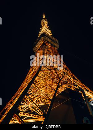 Eine vertikale Low-Angle-Aufnahme des beleuchteten Tokyo Tower im Shiba Park bei Nacht Stockfoto