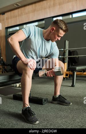 Junger Mann sitzt und trainiert seinen Bizeps mit Kurzhanteln im Health Club Stockfoto