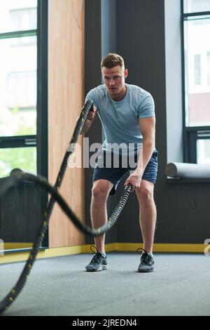 Junger muskulöser Mann macht Übungen mit Seil im Health Club Stockfoto