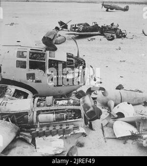 Ein Vintage-Foto um 1942, das einen britischen Bodenbemann zeigt, der einen zerstörten deutschen Heinkel 111-Bomber inspiziert. Im Hintergrund befindet sich ein zerstörtes Messerschmitt BF109-Flugzeug sowie ein RAF-Orkanjäger in der Nähe von El Dabaa, Ägypten, Nordafrika im Zweiten Weltkrieg Stockfoto