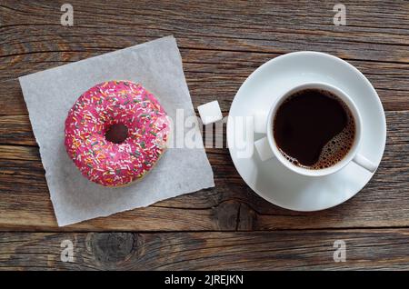Pinkfarbener Donut und Kaffee in der Tasse auf einem alten Holzhintergrund, Draufsicht Stockfoto