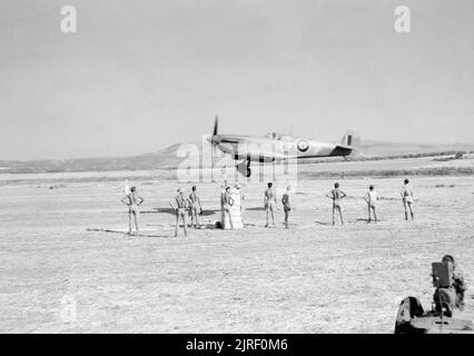 Royal Air Force - Italien, auf dem Balkan und in Südosteuropa, 1942-1945. Personal am Boden zusehen, wie Supermarine Spitfire Mark IX ('UF-?') von Nr. 601 Squadron RAF, kommt im Land auf die neu abgeschlossenen Flugplatz bei Lentini West, Sizilien zu landen. Vier Spitfire Staffeln von Nr. 244 Wing RAF Betrieb vom Flugplatz am darauffolgenden Tag waren. Stockfoto