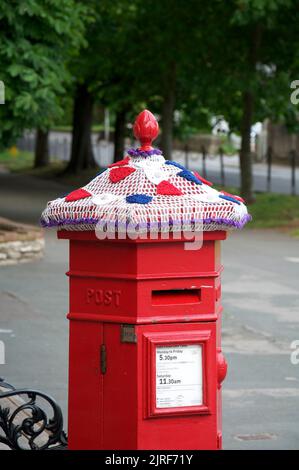 Ein skurriler, farbenfroher, handgestrickter Wollhut ziert eine alte rote viktorianische Säulenbox, die das Platin-Jubiläum von Königin Elizabeth II. Feiert VEREINIGTES KÖNIGREICH. Stockfoto