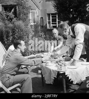 Ein US-Soldat in Tee mit ex-Bürgermeister von Winchester, Herr Edmonds, und seine Frau und seine Tochter im Garten ihres Hauses während 1944. Alfred Miraglia (links, aus New York) dauert Kaffee in der Sonne mit der ex-Bürgermeister von Winchester Herr Edmonds und seine Frau und seine Tochter im Garten ihres Hauses. Die Legende besagt, dass die Edmonds' Kinder, Roger (nicht abgebildet) und Betty, die uns als Gäste der Bürgermeister von Winchester, Virginia eingeladen wurden, und erhielt später einen Teil ihrer Ausbildung dort. Stockfoto