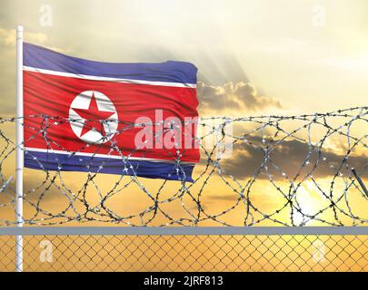 Fahnenmast mit der Flagge Nordkoreas gegen den Himmel und hinter einem Zaun mit Stacheldraht. Das Konzept des Schutzes der Grenzen von Gebieten. Stockfoto