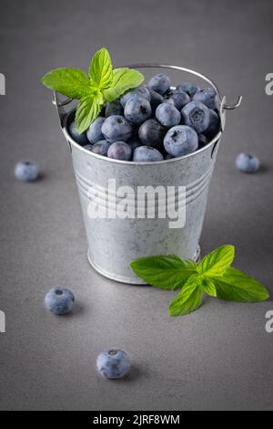 Frische Blaubeeren in kleinem Eimer auf dem grauen Tisch Stockfoto