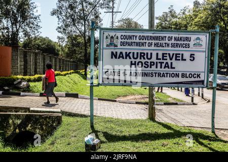 Eine Frau kommt an einer Schild-Tafel des Nakuru Level 5 Krankenhauses in der Stadt Nakuru vorbei, wo zwei Kinder, die vom Schweinegrippe-Virus (H1N1) betroffen sind, aufgenommen werden. Die Regierung sagt, dass sie einen Ausbruch der Schweinegrippe (H1N1) im Dorf Kiptangwanyi eingedämmt hat. Die Viruserkrankung hat das Leben eines Kindes beansprucht und 8 weitere im Nakuru Level 5 und im Kiptangwanyi Health Center in Elementtaita ward aufgenommen. Stockfoto