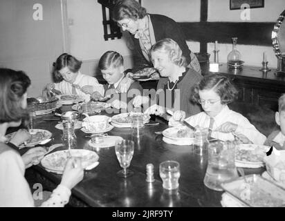 Frau Carter genießt das Mittagessen am Sonntag mit Ihrem evakuiert Kinder Michael und Angela während einem Ausflug in ihrer Pflegefamilie in Haywards Heath im Jahre 1940. Frau Carter genießt ein Mittagessen am Sonntag mit Ihrem evakuiert Kinder Michael und Angela (entweder Seite ihr am Tisch sitzend) während einer Reise zu ihrer Pflegefamilie in Haywards Heath. Die Kinder wurden von ihrem Haus in London evakuiert und bleiben mit mehreren anderen Evakuierten in die Heimat von Frau Cluton, hier gesehen, die Kartoffeln zu Michael. Stockfoto