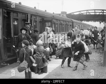 Eine Gruppe von Kindern an Brent Station in der Nähe von Kingsbridge, Devon, nachdem Sie von Bristol 1940 evakuiert. Eine Gruppe von Kindern ankommen auf einer Plattform an Brent Station, in der Nähe von Kingsbridge, Devon, nachdem Sie von Bristol 1940 evakuiert. Der Zug auf, die Sie zurückgelegt haben, können klar Neben gesehen werden. Die Kinder tragen Taschen, Koffer, oder Bündel von Kleidung und haben auch ihre Gasmasken mit Ihnen. Die Schutzvorrichtung vom Bahnhof und viele der weiblichen Freiwilligen, die geholfen zu begleiten diese Kinder nach Devon auch gesehen werden kann. Stockfoto