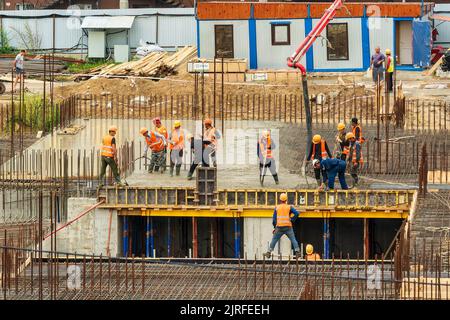 RUSSLAND, KALUGA - 15. AUGUST 2022 : Betonautomatisches Pumpenrohr, das auf der Baustelle arbeitet. Gruppe von Arbeitern, die Beton leiten und gießen. Stockfoto