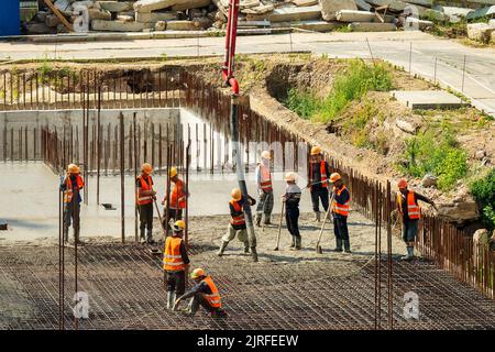 RUSSLAND, KALUGA - 15. AUGUST 2022 : Betonautomatisches Pumpenrohr, das auf der Baustelle arbeitet. Gruppe von Arbeitern, die Beton leiten und gießen. Stockfoto