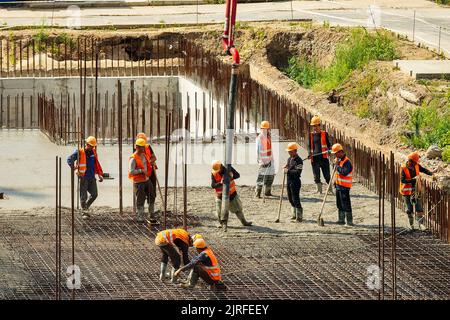 RUSSLAND, KALUGA - 15. AUGUST 2022 : Betonautomatisches Pumpenrohr, das auf der Baustelle arbeitet. Gruppe von Arbeitern, die Beton leiten und gießen. Stockfoto