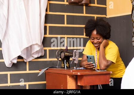 Weibliche afrikanische Schneiderin überprüft ihr Telefon Stockfoto