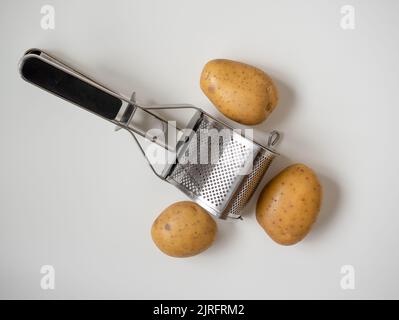 Robuster mechanischer Hand-Kartoffelstampfer aus Edelstahl mit Maris Piper-Kartoffeln Stockfoto