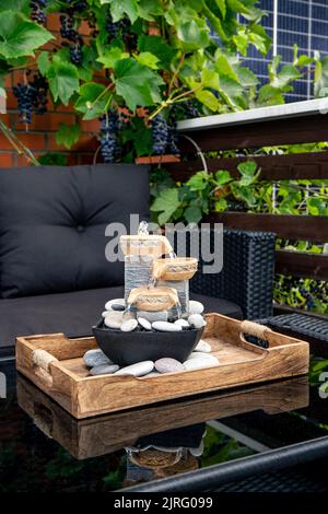 Home Terrasse mit schwarzen Kunststoff-Gartenmöbel, kleine entspannende elektrische Zen-Tisch Brunnen auf dem Tisch und echte Weinreben mit Trauben hängen. Stockfoto