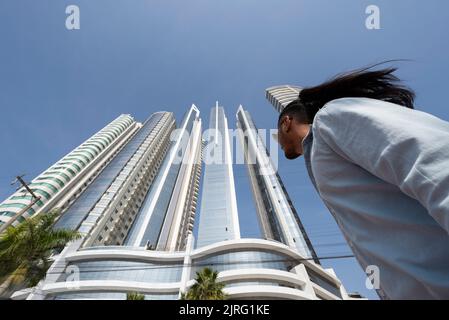 Balneário Camboriú, Santa Catarina, Brasilien - 28. Juli 2022: Mann in legerer Kleidung, der die Atlântica Avenue vor Wolkenkratzern spazierengeht Stockfoto