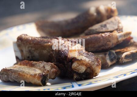 Nahaufnahme mit defokussiertem Hintergrund von Schweinerippen, die auf einem Holzgrill gegart wurden Stockfoto