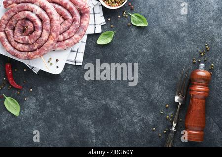 Rohe, spiralförmige Schweinswürste. Frische Schweinswürste leckere Spirale zum grillen auf weißem Ständer mit Gewürzen und Kräutern zum Oktoberfest Party Dinner auf grauem B Stockfoto