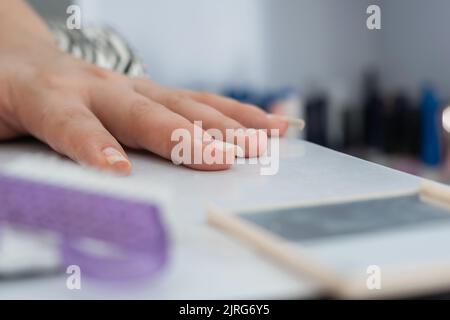 Alle de la mano de una chica latina, colocada en la mesa de manicura, lista para empezar a pintar y decorar las uñas. En el fondo muchos esmaltes d Stockfoto