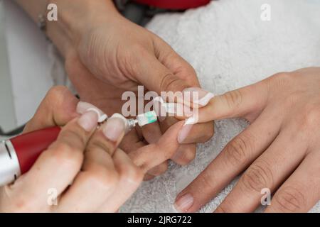 Detail der Hand der Manikuristin, die den Finger einer Frau hält, während sie ihren Nagel mit dem elektrischen Nagelpuffer schleift, ideal zum Polieren von Acryl- und Gelnägeln. G Stockfoto