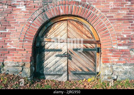 An Bord eines alten Schlosses aus Ziegelsteinen, das von Herbstlaub überschwemmt wurde, wurden Holztore aufgefahren Stockfoto