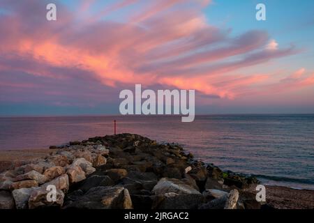 Wunderschöne, wispy rote Wolken über dem West Bay Strand in Dorset, England, Großbritannien Stockfoto