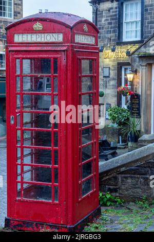 Eine rote Telefondose oben auf der Main Street, Haworth, Yorkshire. Die Box befindet sich vor dem Black Bull Pub, das Bild wurde im Abendlicht aufgenommen. Stockfoto