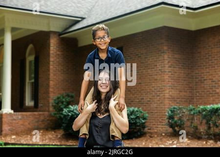 Eine große Schwester hält ihren kleinen Bruder auf den Schultern für ein lustiges Porträt Stockfoto