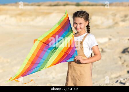 Ein Mädchen in einem Sommerkleid lässt einen Drachen wild in den Himmel steigen. Stockfoto