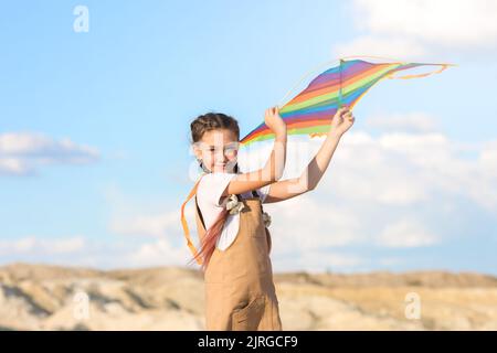 Ein Mädchen im Sommerkleid startet einen Drachen in den Himmel in freier Wildbahn. Stockfoto